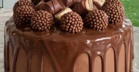 Rich chocolate drip cake decorated with chocolate ganache, chocolate candies, crispy chocolate balls, and macarons.