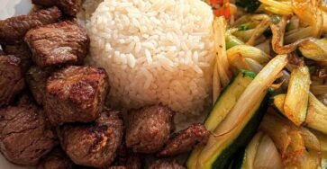 Bistec estilo hibachi con arroz blanco, arroz frito con verduras y calabacín salteado con cebolla en un plato.