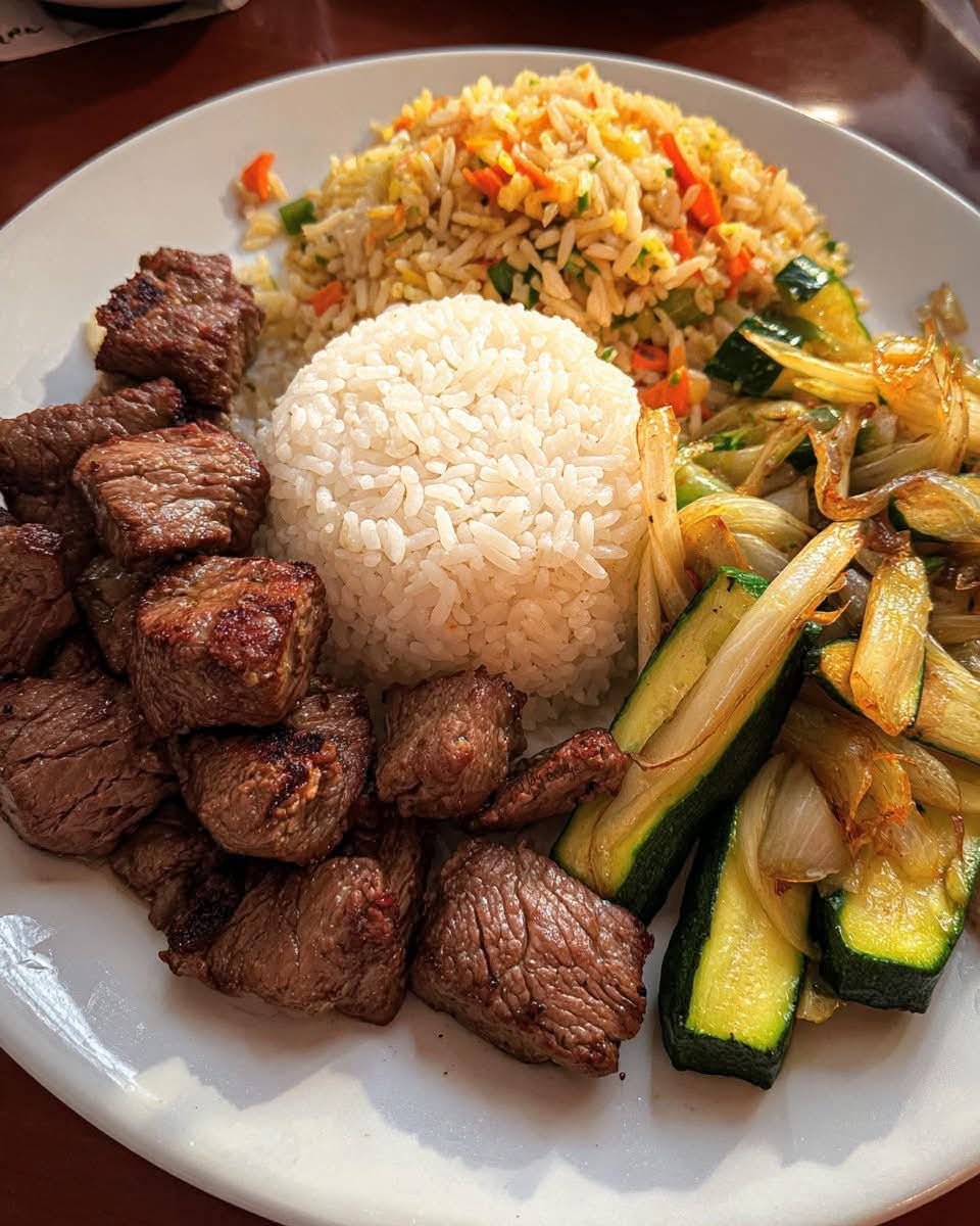 Bistec estilo hibachi con arroz blanco, arroz frito con verduras y calabacín salteado con cebolla en un plato.