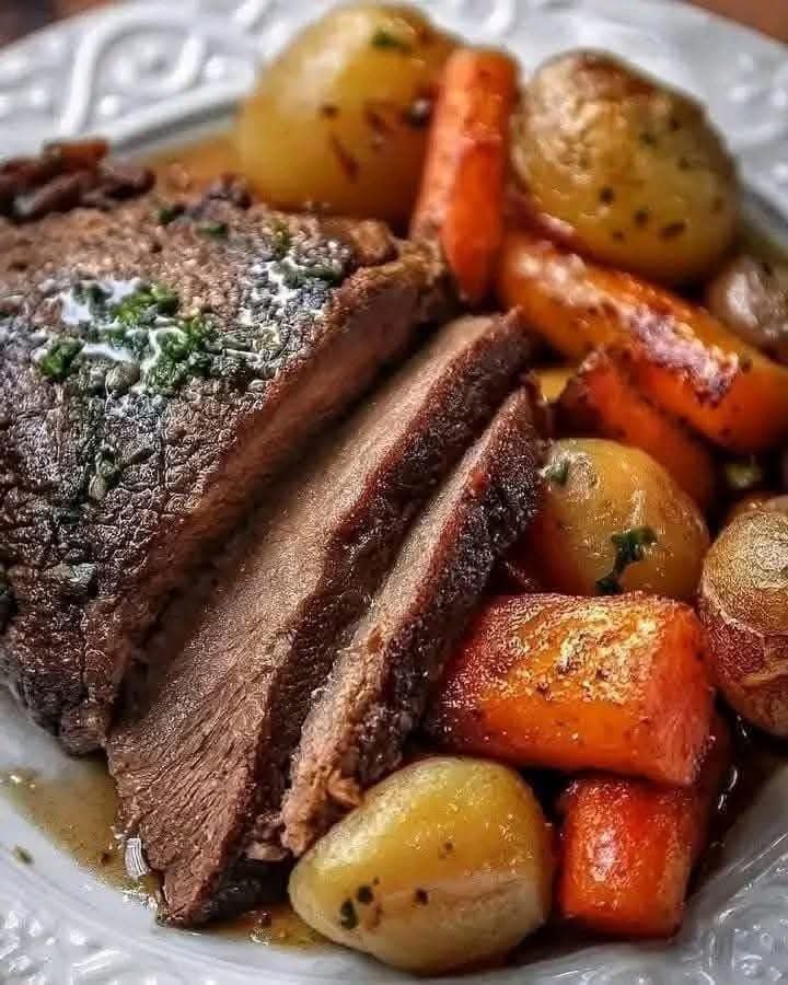 Tender classic pot roast with roasted potatoes and carrots served with rich beef gravy and fresh parsley on a white dinner plate.