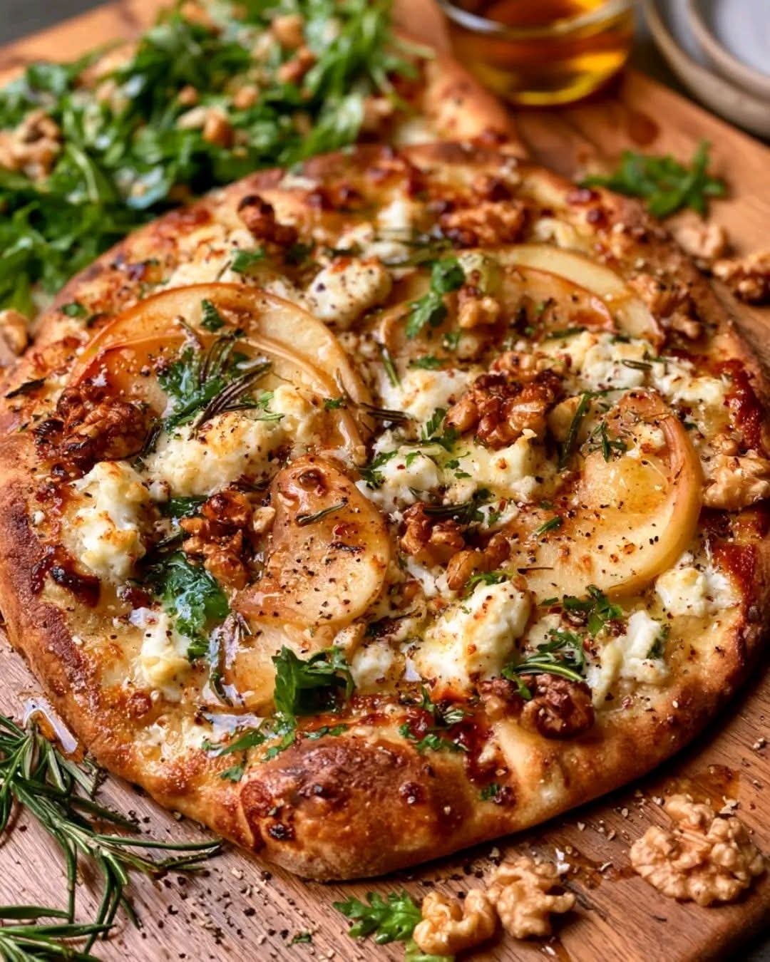 Homemade apple feta walnut flatbread topped with fresh rosemary, toasted walnuts, arugula, and honey drizzle on a crispy artisan crust.