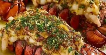 Grilled garlic butter lobster tails topped with Parmesan, fresh parsley, and herbs, served with lemon wedges.