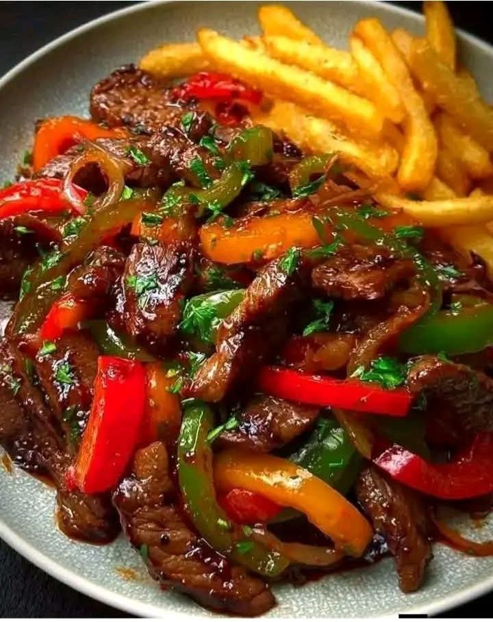 Sizzling beef stir-fry with colorful bell peppers, onions, and crispy French fries served on a plate for an easy homemade dinner.