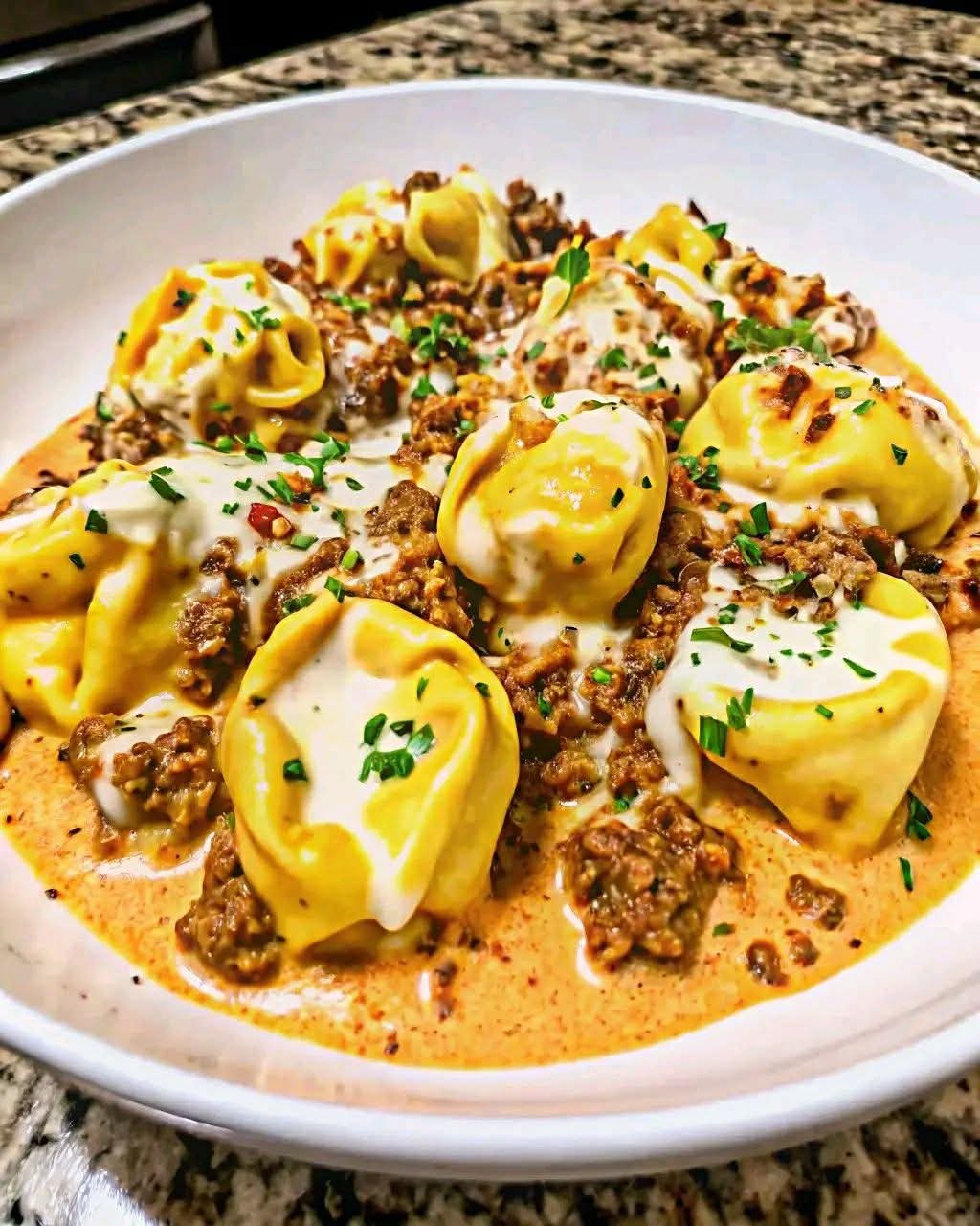 Cheesy garlic beef tortellini served in a creamy Parmesan mozzarella sauce, garnished with fresh parsley in a white bowl.