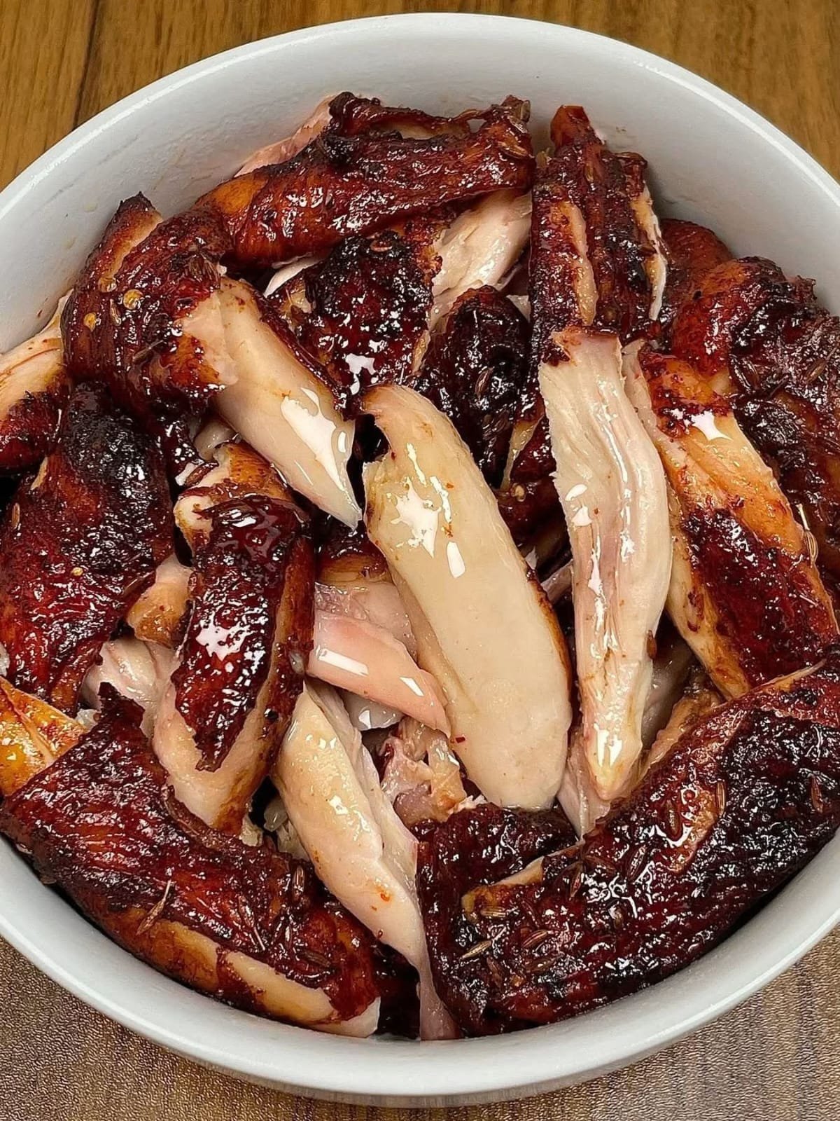 Juicy glazed roasted chicken pieces with crispy caramelized skin served in a white bowl.