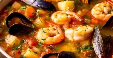 Bowl of hearty coastal seafood soup with shrimp, mussels, white fish, potatoes, tomatoes, and fresh parsley.