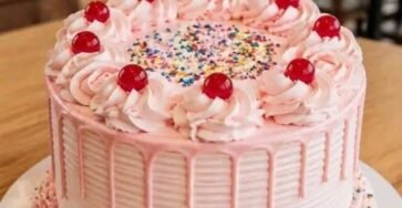 Pastel de fresa con buttercream rosa, drip de chocolate blanco, cerezas y chispas de colores