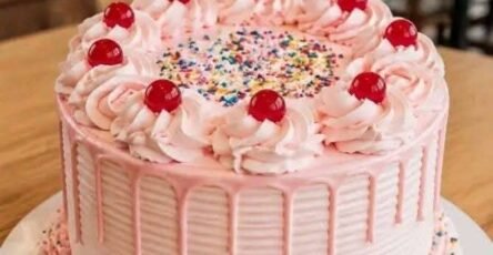Pastel de fresa con buttercream rosa, drip de chocolate blanco, cerezas y chispas de colores